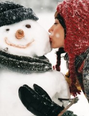 картинка Девушка и снеговик - Красивая девушка в шапке красного цвета целует в щёку снеговика, закрыв при этом глаза, для мобильного телефона